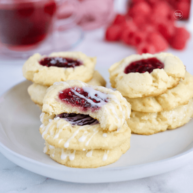 Raspberry Thumbprint Cheesecake Cookies on plate with raspberries and tea in background.