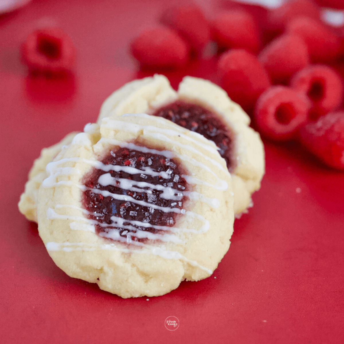 5-ingredient Raspberry Thumbprint Cheesecake Cookies with fresh raspberries in background.