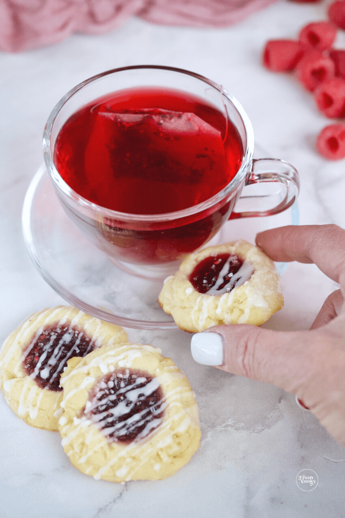 Serving raspberry thumbprint cheesecake cookies with bright red hot cup of tea.