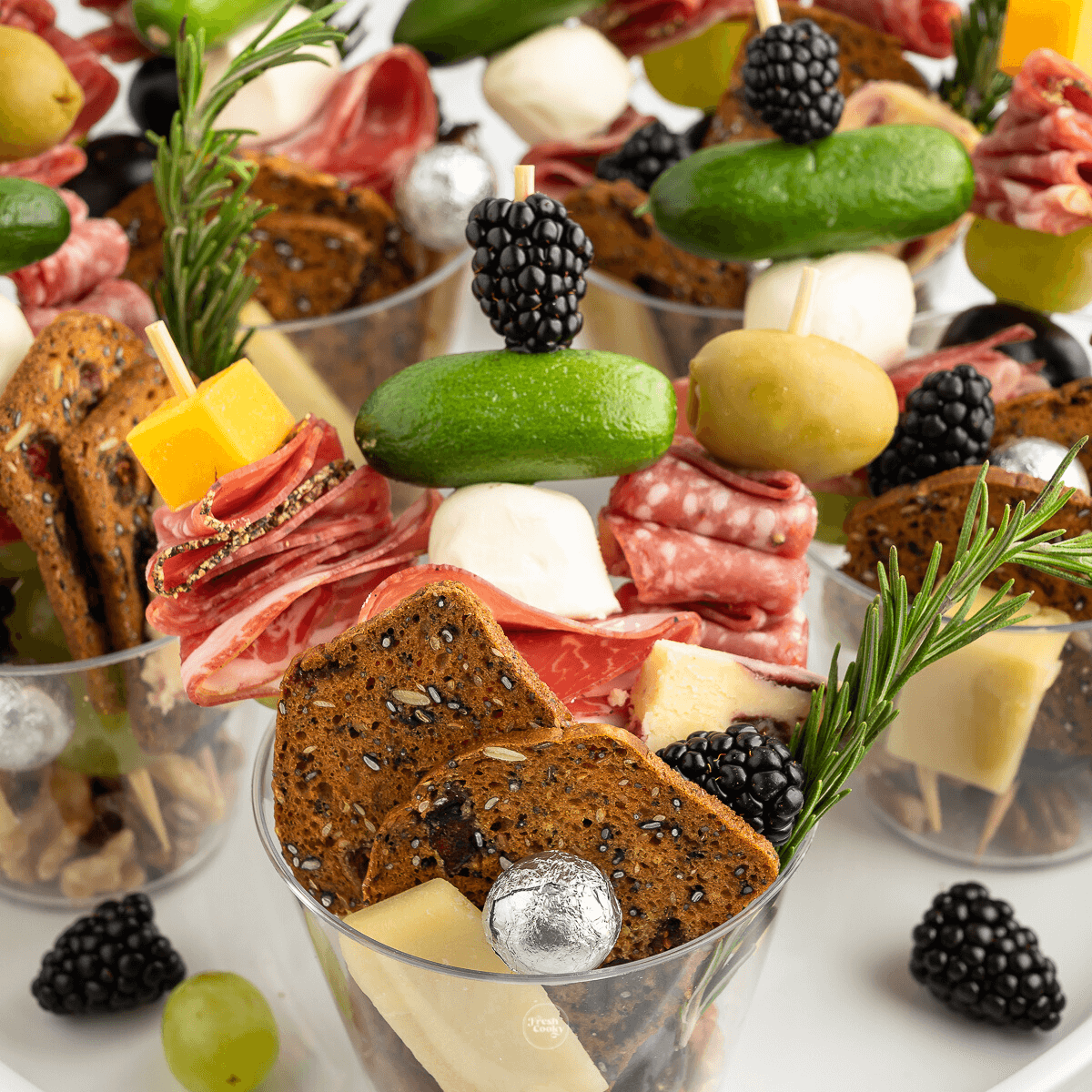 Multiple charcuterie cups loaded with cured meats, cheese, chocolates, fruit and veggies.