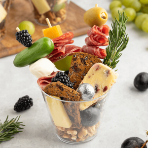 Charcuterie cup filled with cured meats, cheese, veggies on skewersand nuts and crackers.