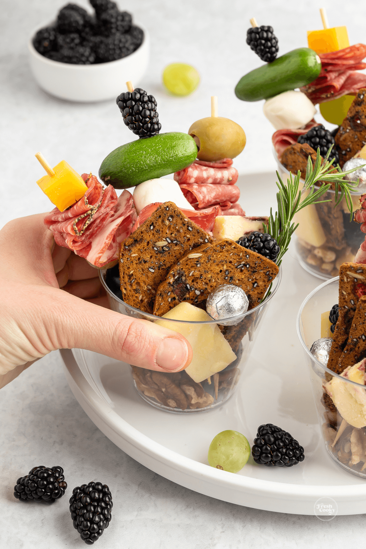 Hand grabbing a charcuterie cup off of a tray.