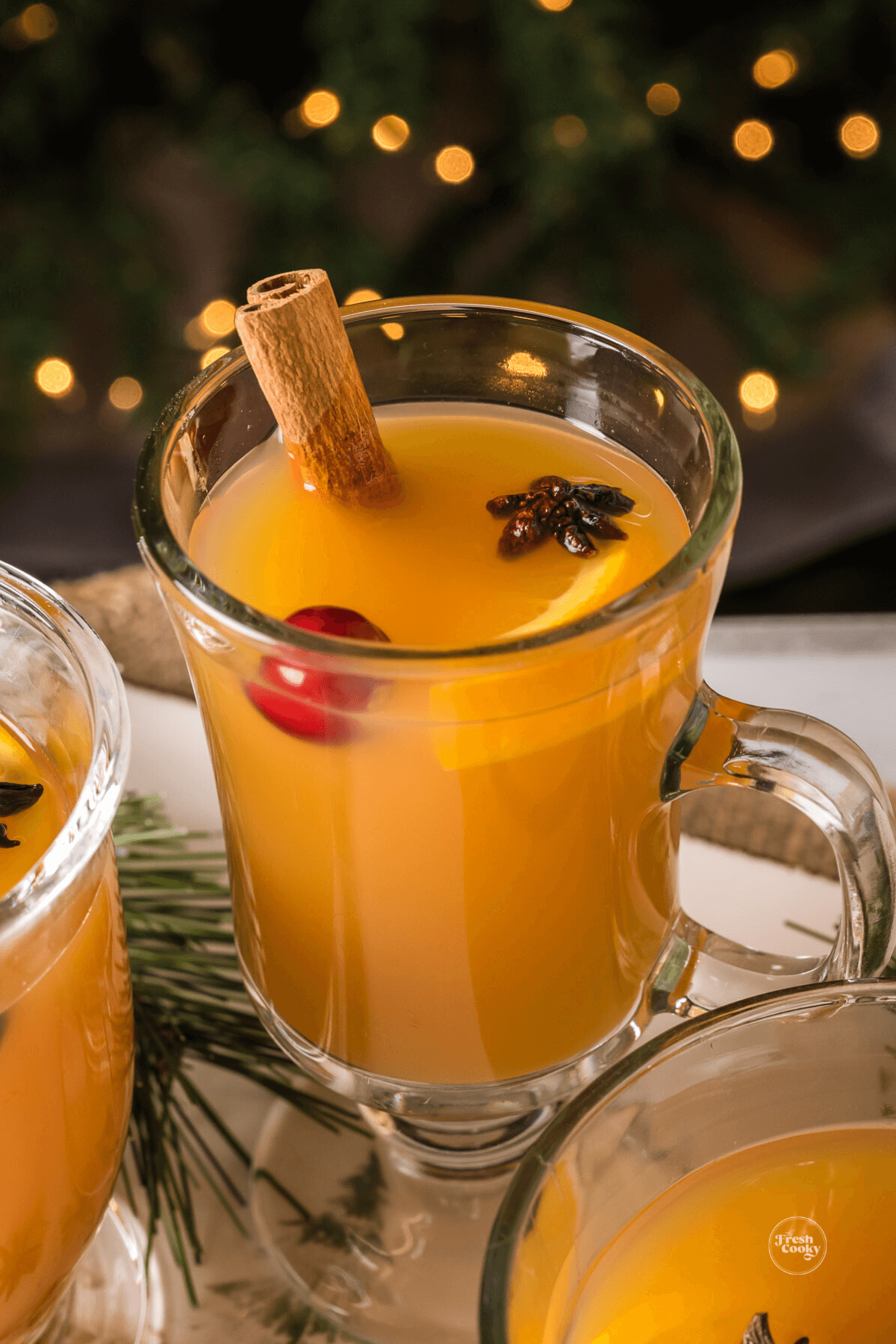 Cozy hot mulled wassail in glass mugs in front of Christmas tree.