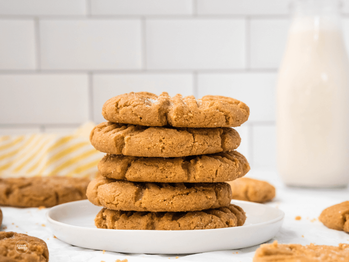 Stacked peanut butter cookies gluten-free with jar of milk in background.