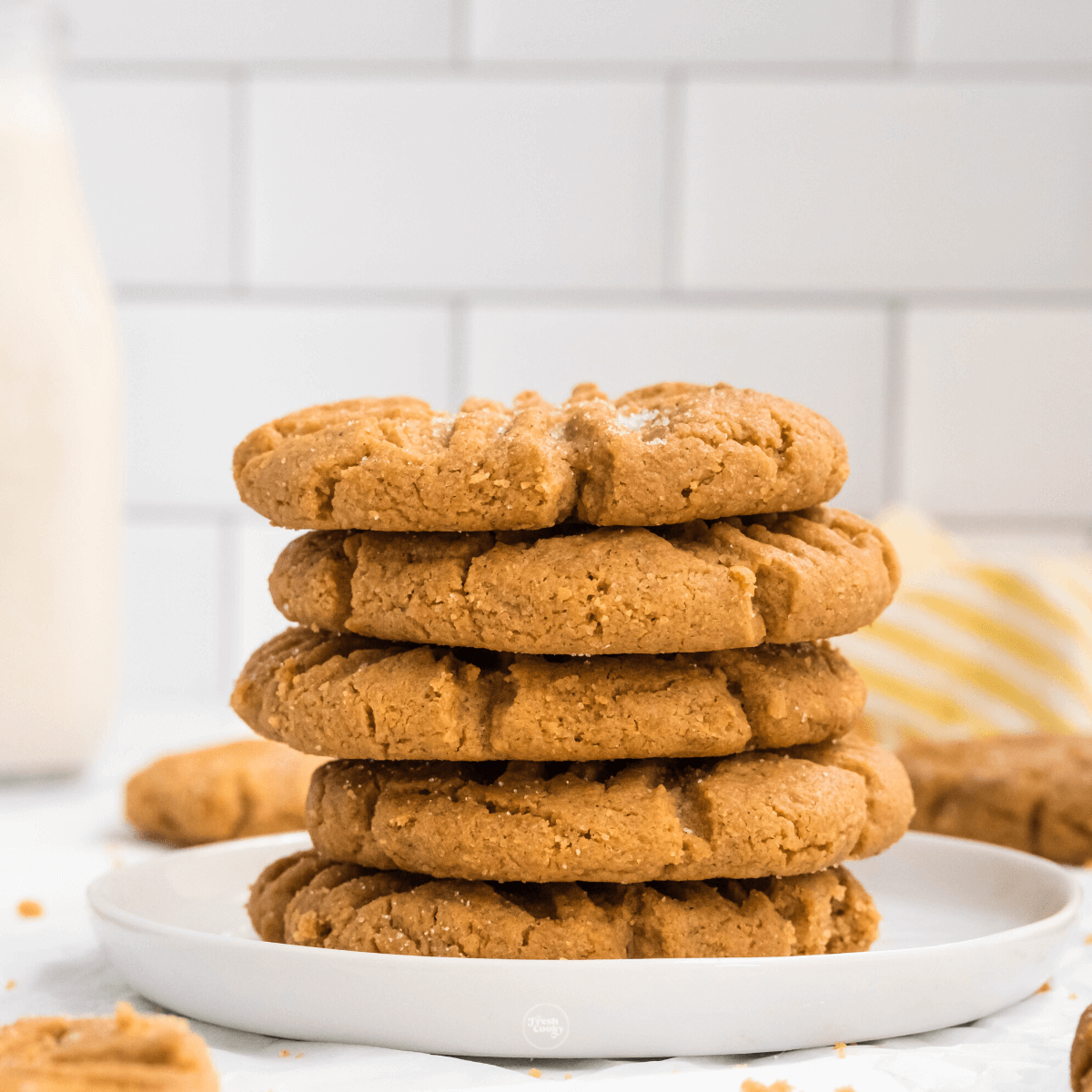 Peanut Butter cookies stacked on plate with glass of milk in background.