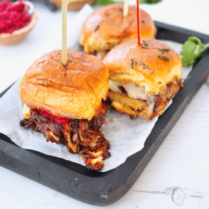 Three roast beef sliders on a tray with a cocktail pick in the top.