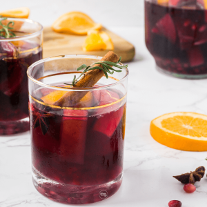 Spiced Holiday Sangria in pretty glass garnished with cinnamon stick and sprig of rosemary.