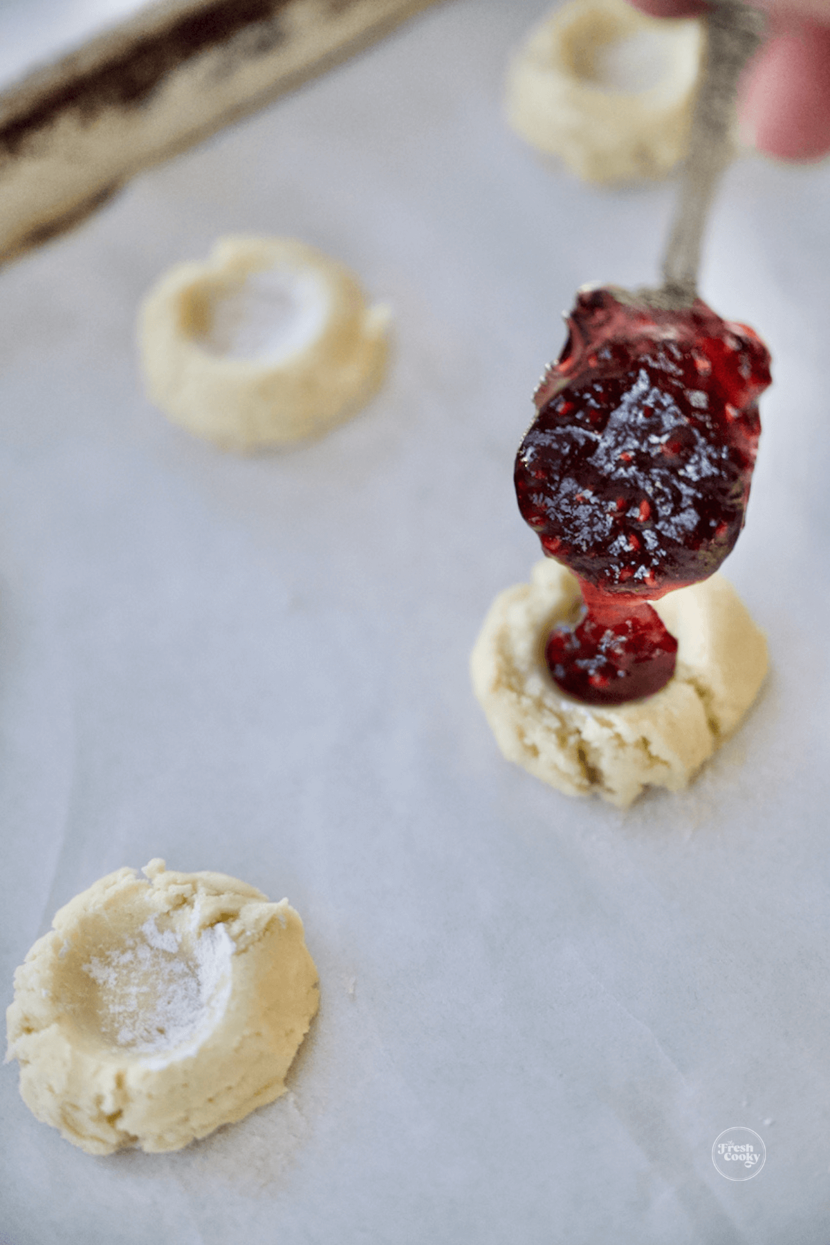 Adding small dollop of raspberry preserves to cookies.