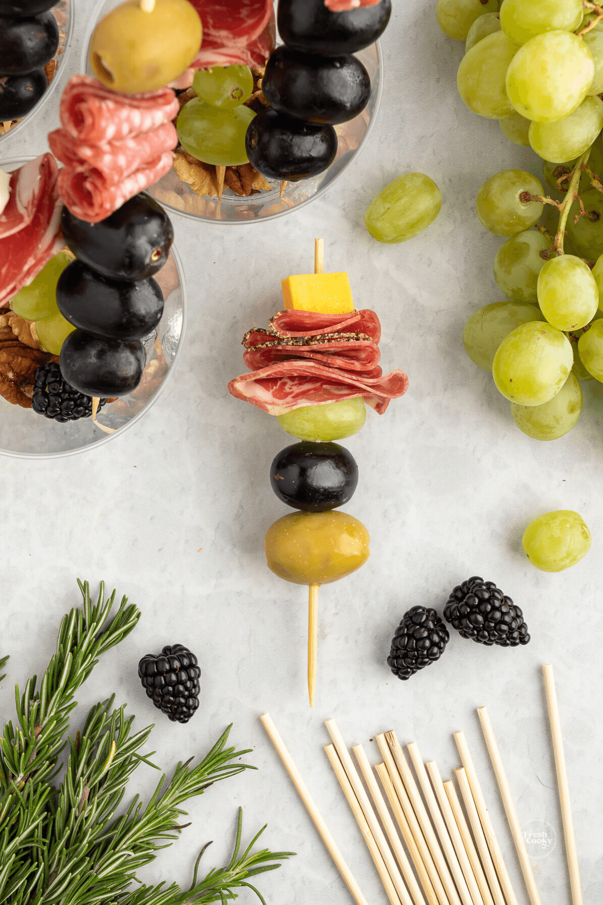 Layering fruit, meat, cheese and olives on skewer.