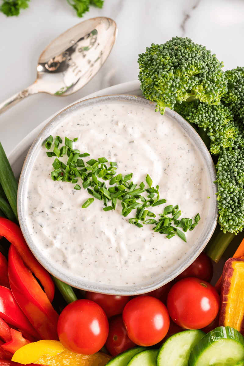 Lovely veggie dip in rustic bowl garnished with chopped chives with fresh veggies surrounding the dip.