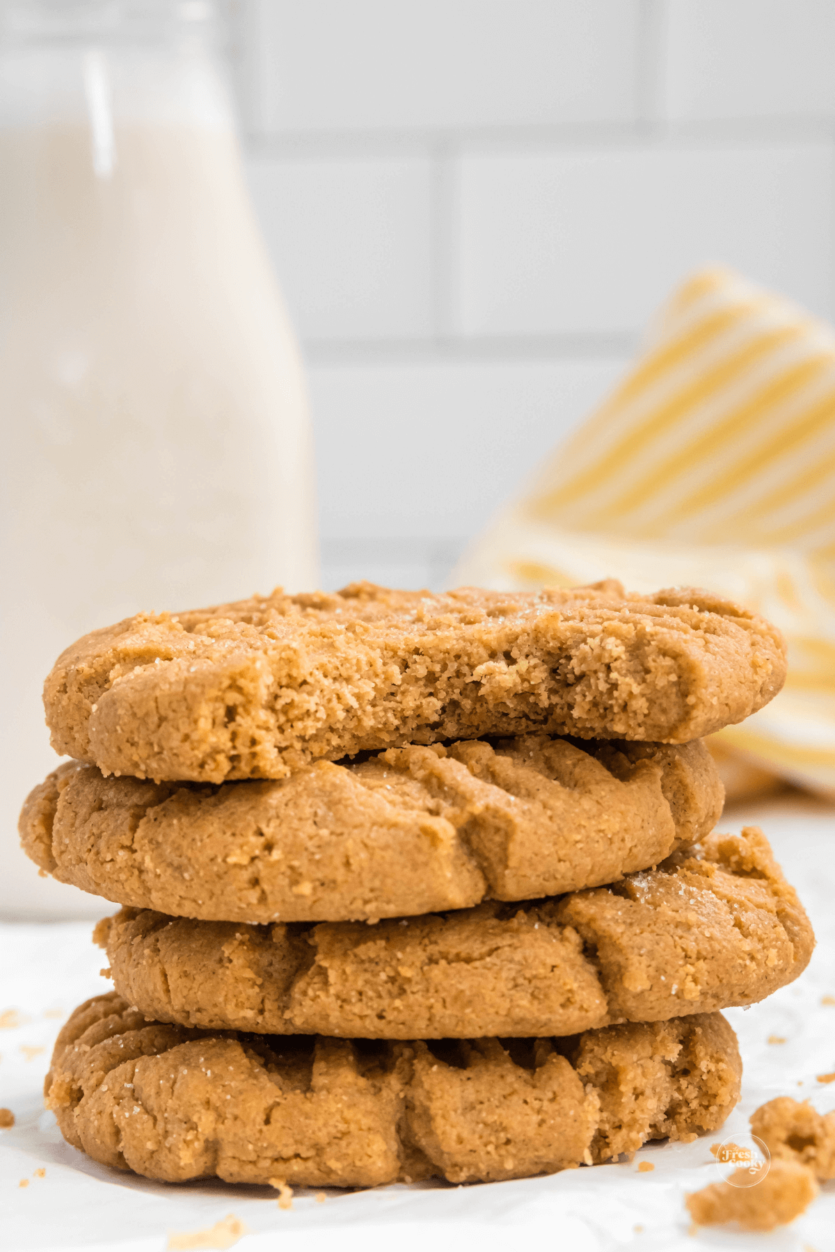 Peanut Butter cookies stacked with bite taken and milk in background.