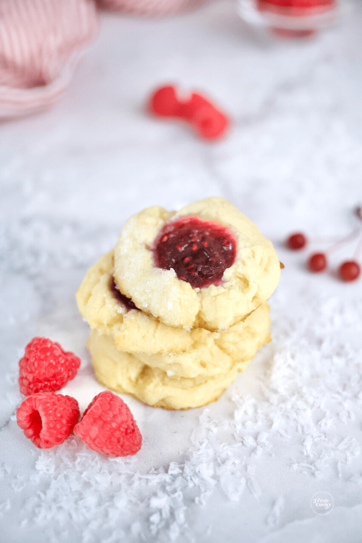 Raspberry thumbprint cookies stacked with fresh raspberries nearby.