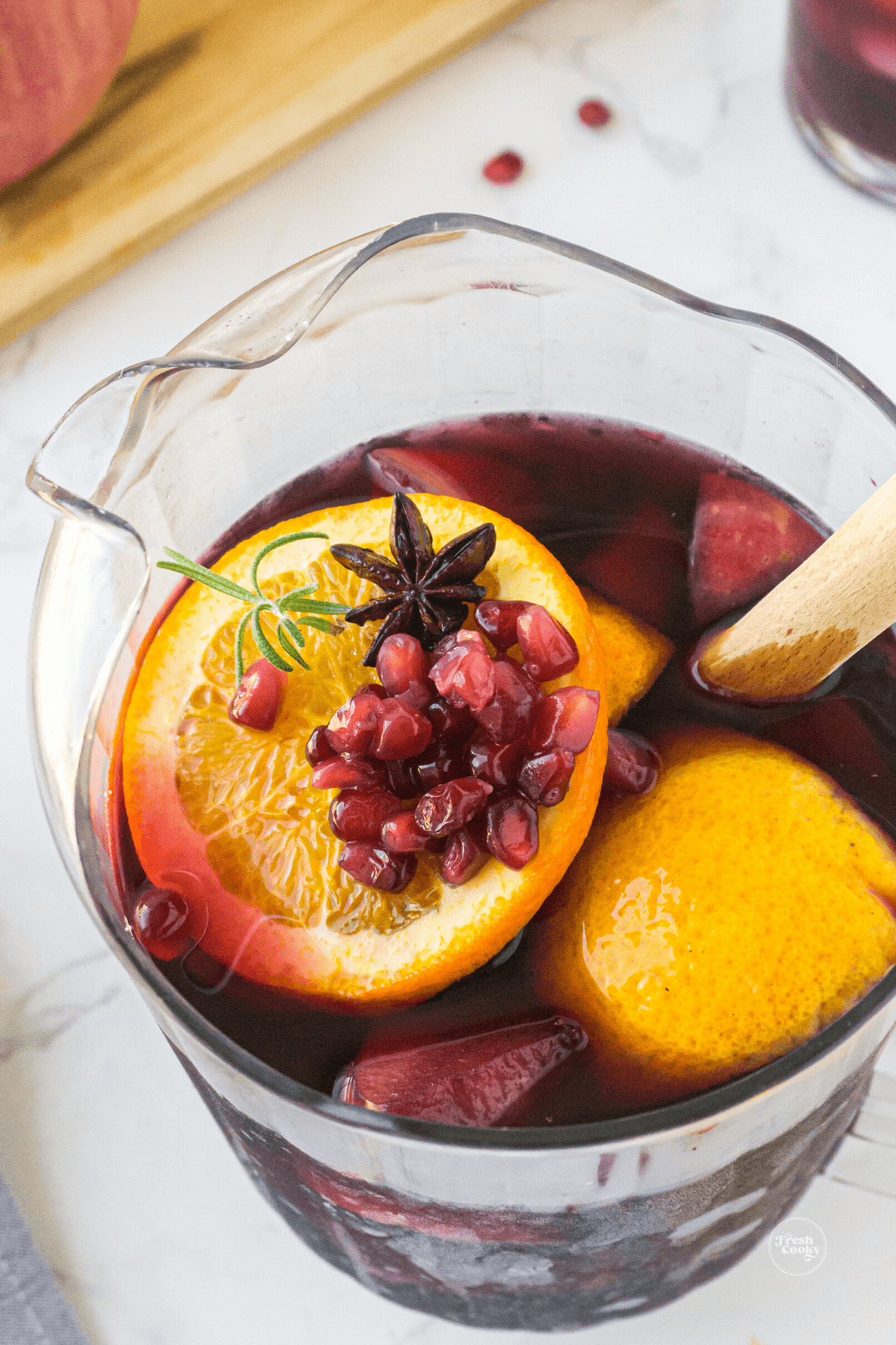 Red wine for sangria poured into pitcher filled with fruit, spices and rosemary. 