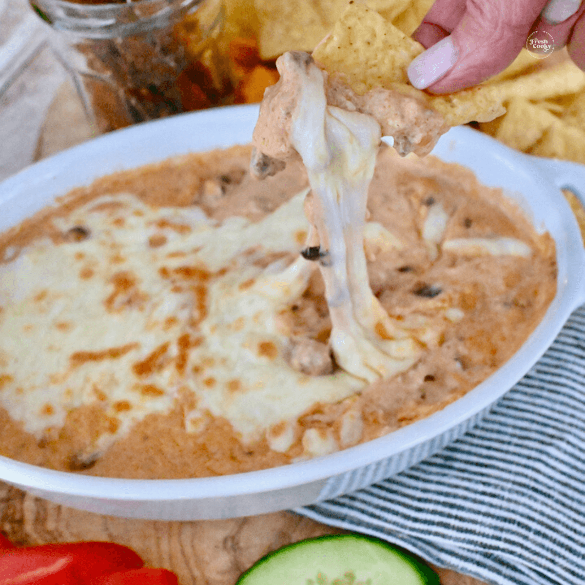 Easy 3 Ingredient Chili Cheese Dip with hand scooping stringy cheesy chili dip onto a chip.