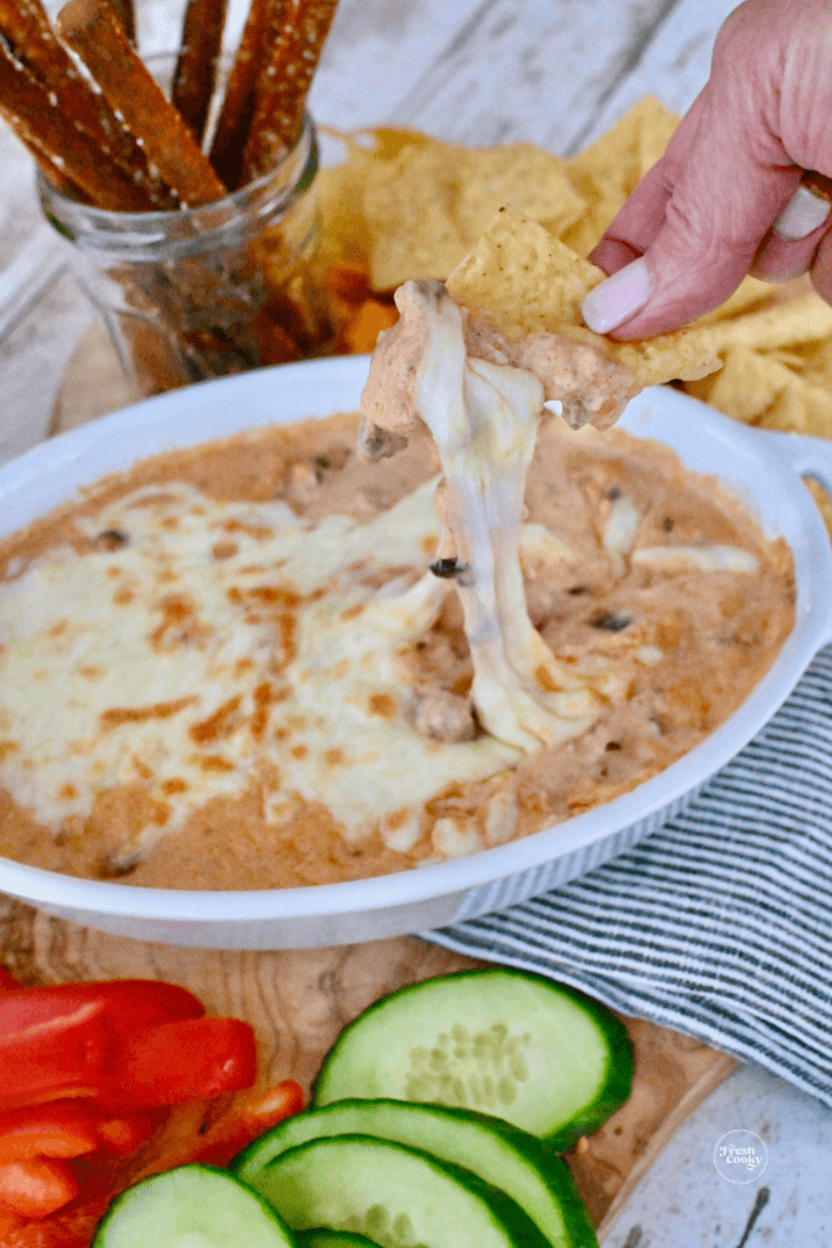 Chili cheese dip with hand dipping into stringy cheese with a tortilla chip. 