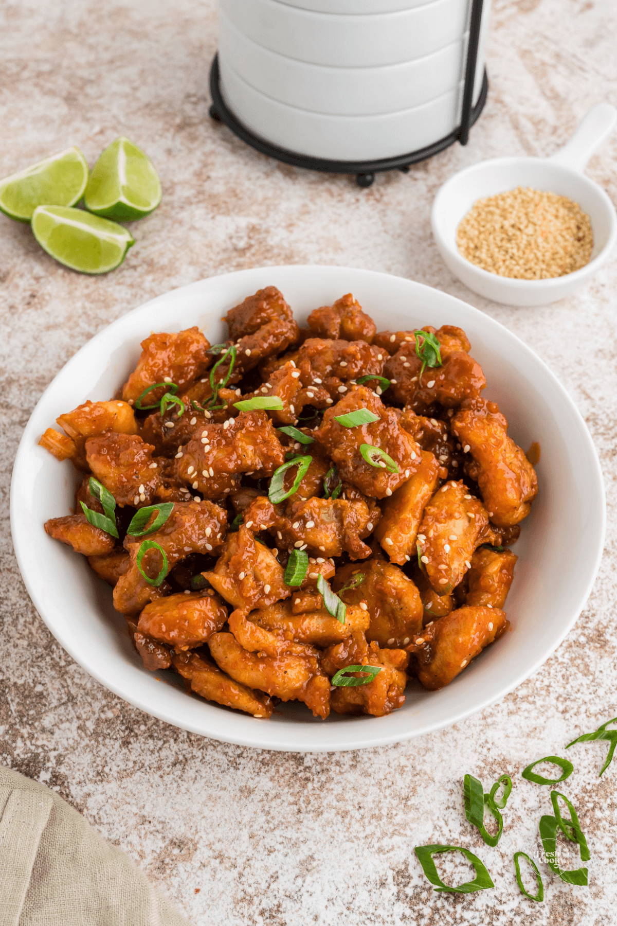 Air fryer Korean Chicken, extra crispy in large bowl garnished with sesame seeds, lime and scallions.