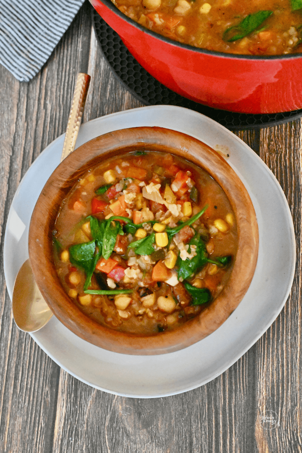 Wooden bowl filled with serving of copycat Panera Bread 10 vegetable soup, with Dutch oven in background.