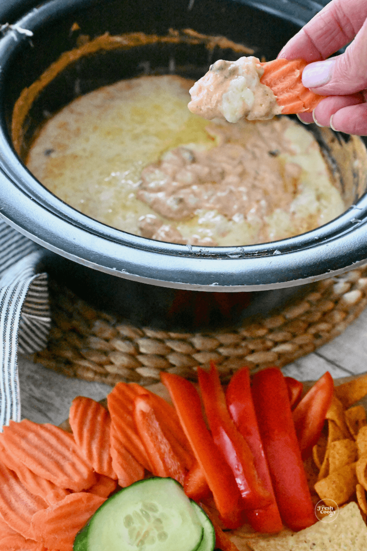 3 ingredient chili cheese dip crock pot with hand using carrot chip to scoop some of the dip.