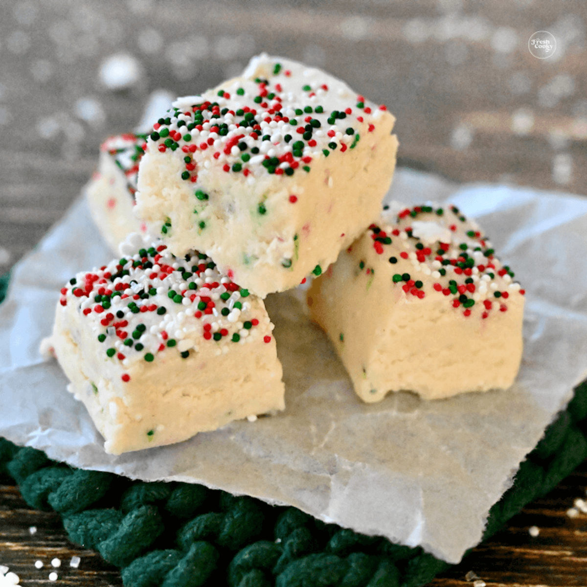 Christmas Cookie Fudge Recipe pieces on parchment with holiday sprinkles.