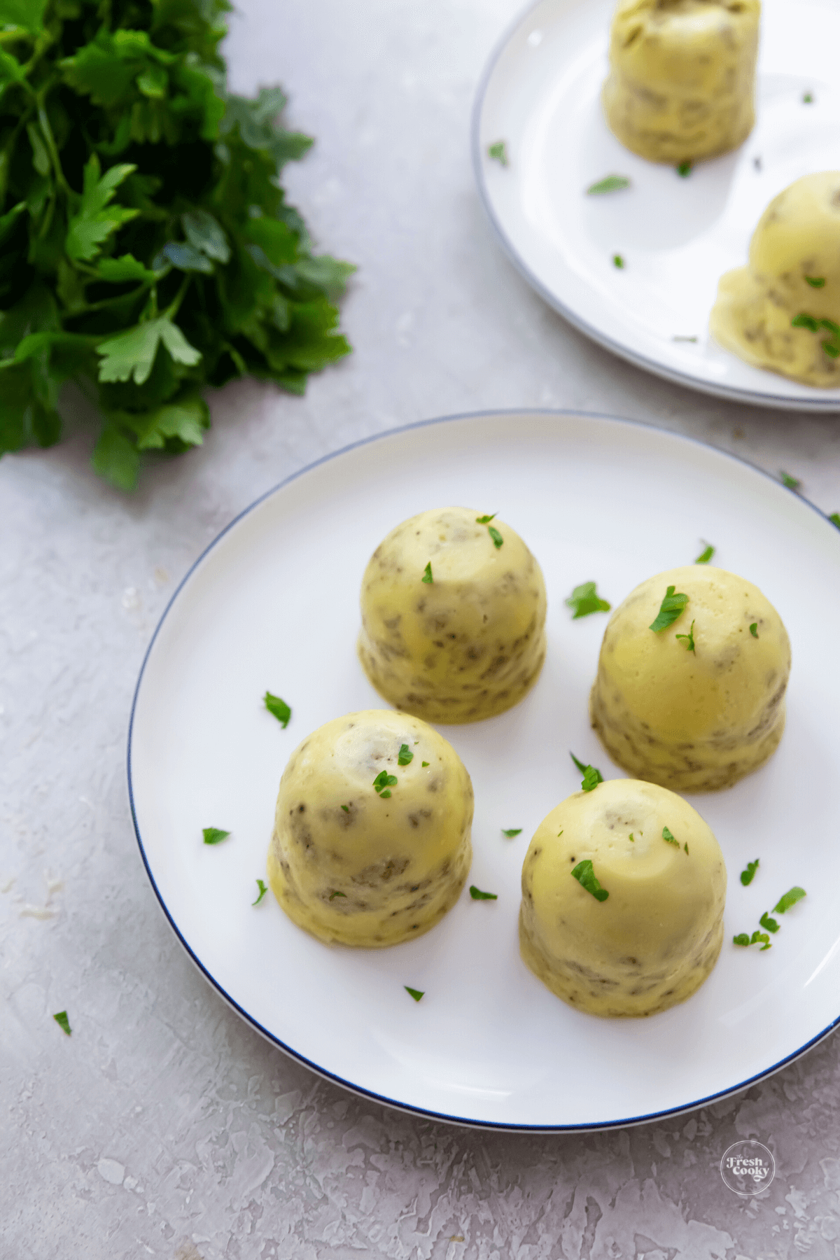 Egg bites on plates with some fresh parsley nearby.