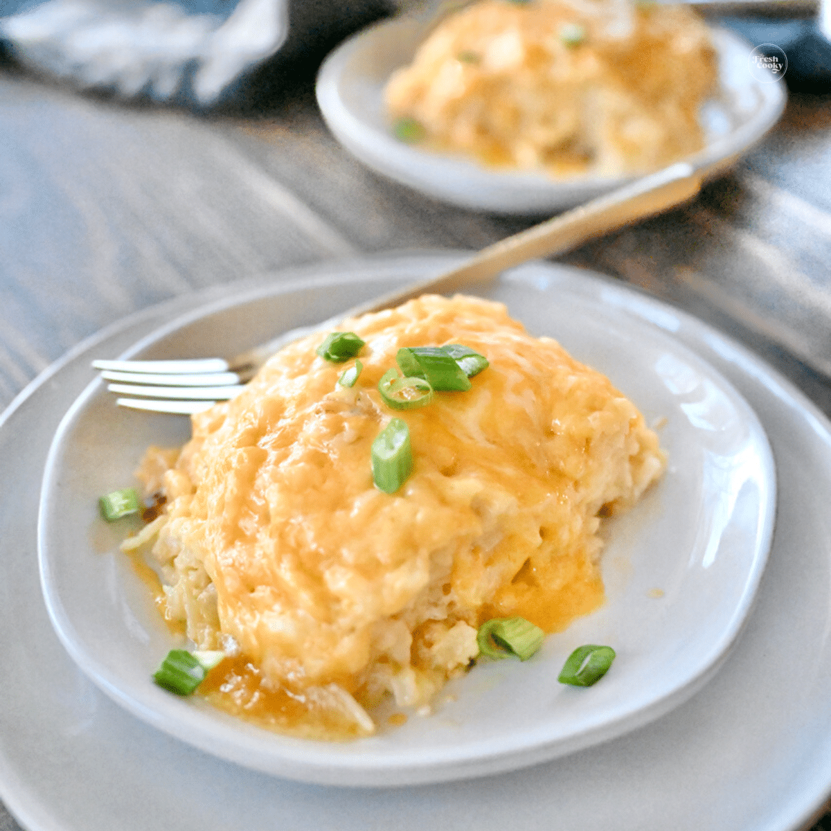 Large serving of cracker barrel hashbrown casserole on plate garnished with green onions.