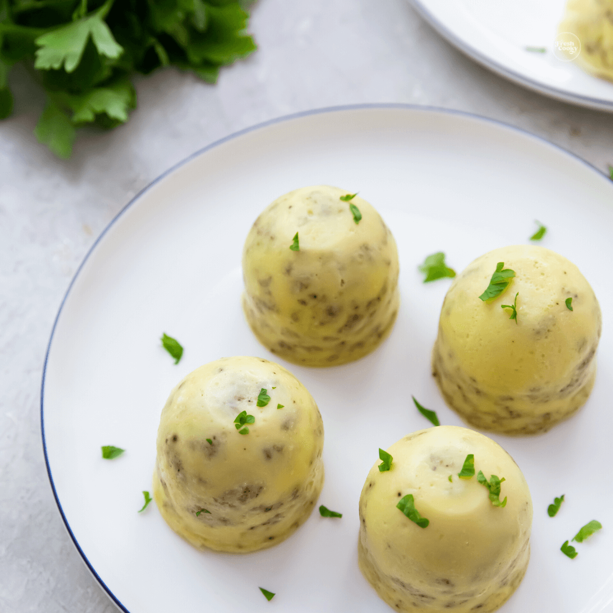 Four egg bites on a plate sprinkled with parsley.