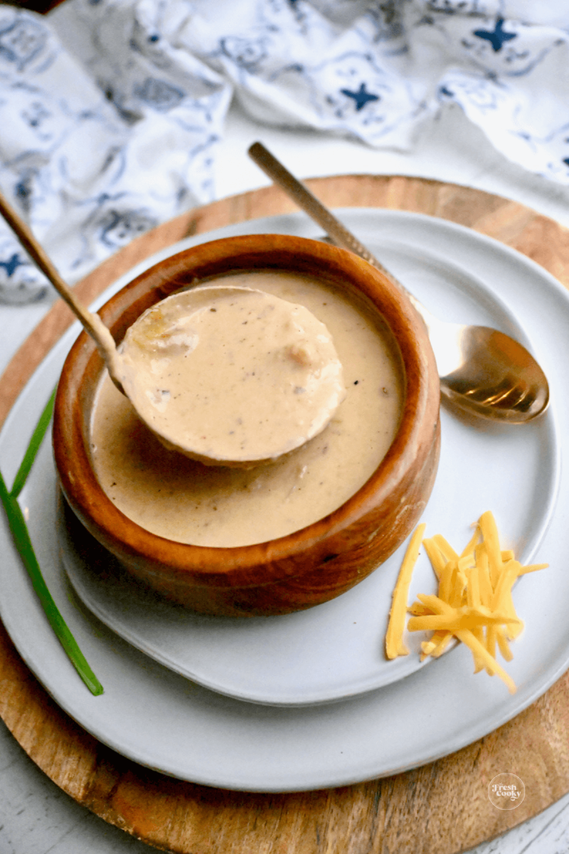 Ladling potato soup into wooden bowl.