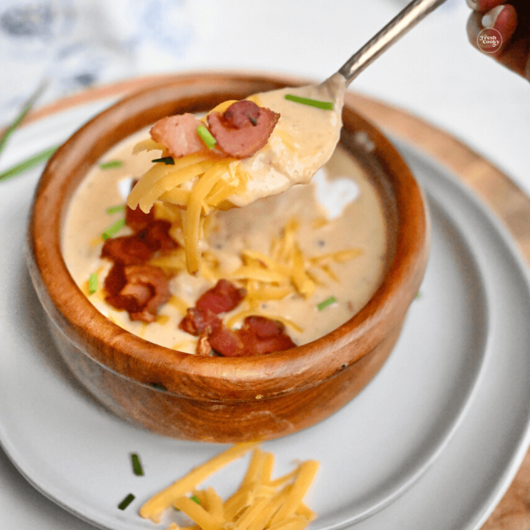 Loaded baked potato soup in wooden bowl, topped with bacon, shredded cheddar and sour cream.