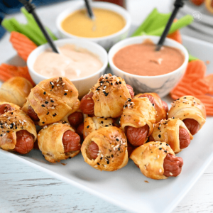 Air fryer pigs in a blanket on a plate with three sauces for dipping.
