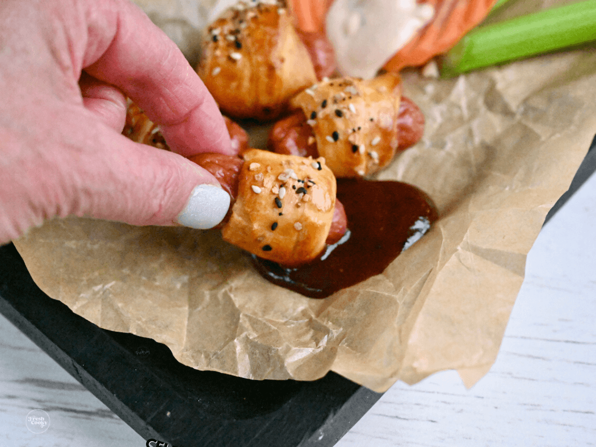 Hand dipping pig in blanket into sauce.