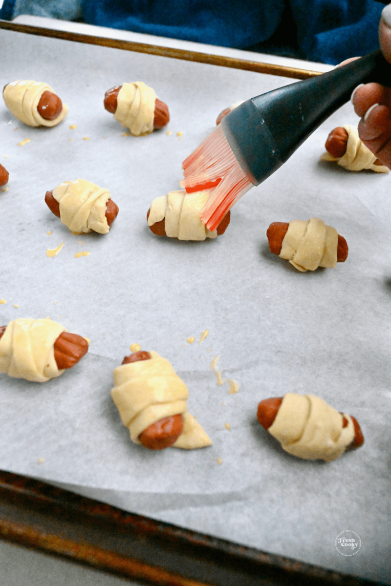 Brushing egg wash onto pigs in blankets.