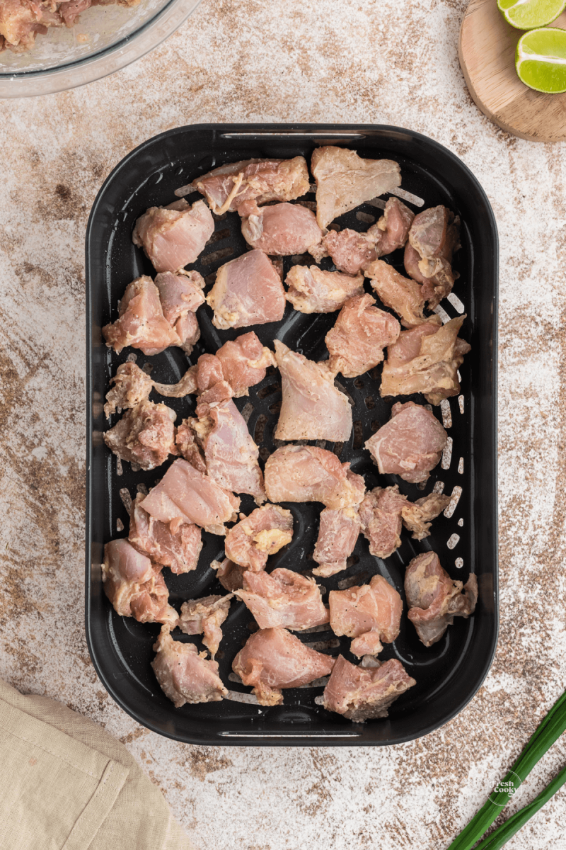 Single layer of seasoned chicken thighs in air fryer basket.