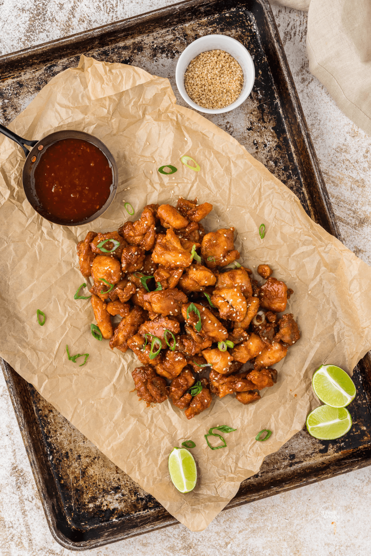 Fried chicken with Korean BBQ sauce on parchment paper and baking sheet with sauce and garnish.