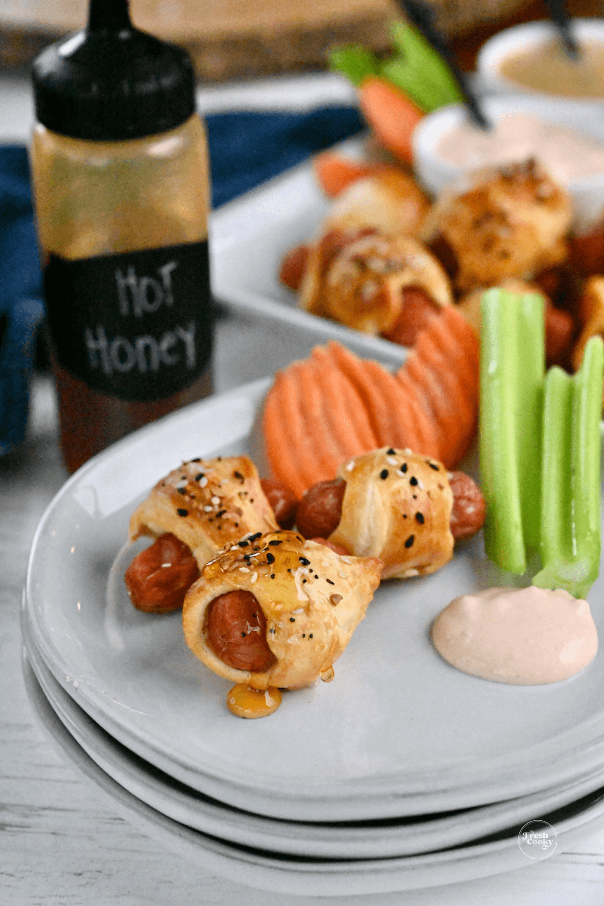 Pigs in a blanket on plate with hot honey, veggies and dipping sauce. 