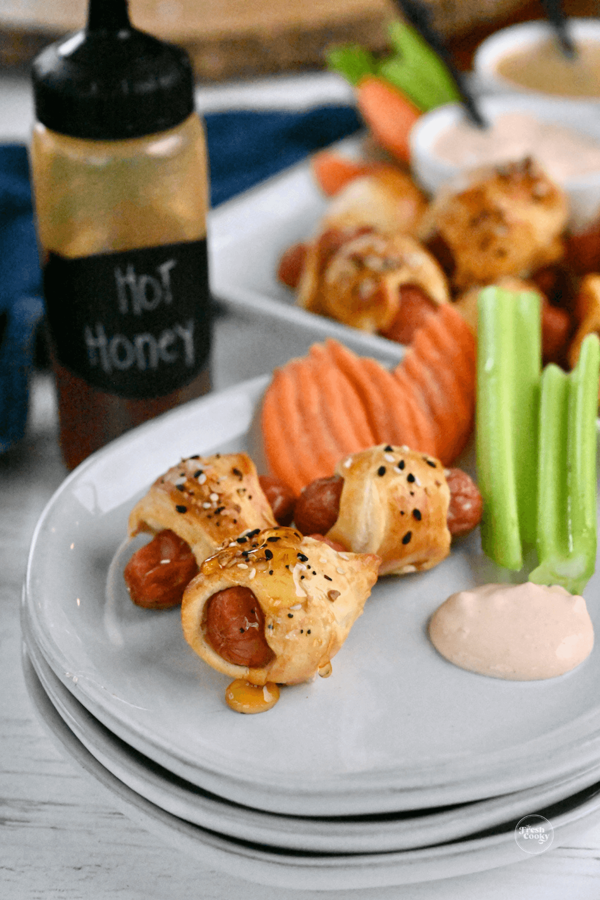 Pigs in a blanket on plate with hot honey, veggies and dipping sauce.