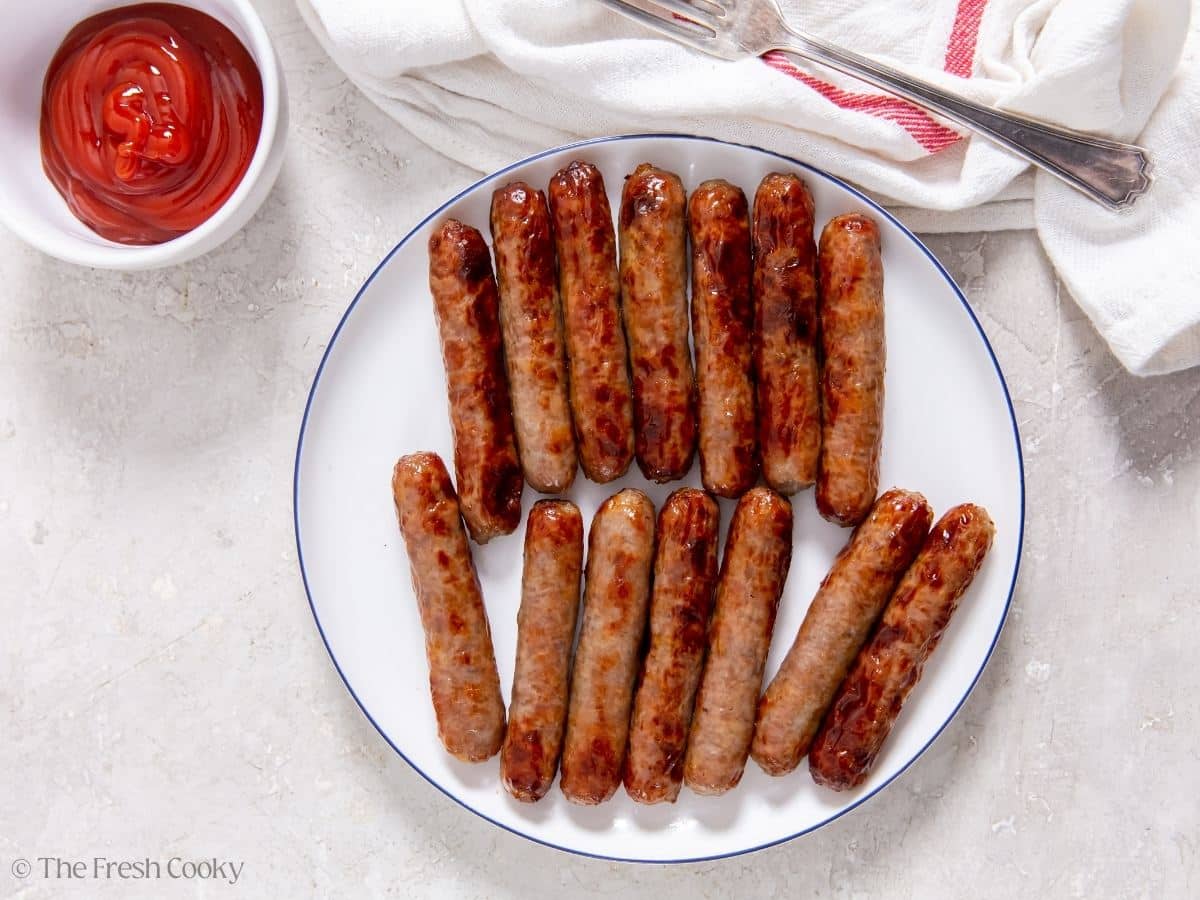 Air fried sausage links on a plate with ketchup nearby.