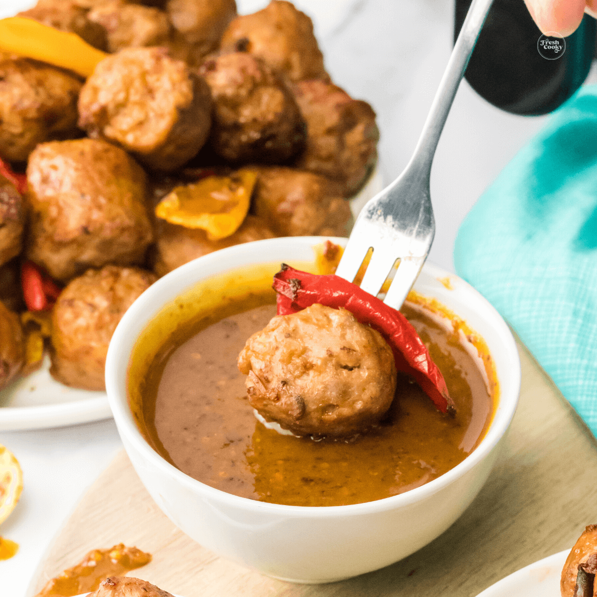 Fork with sausage bite, dipping into spicy mustard sauce.