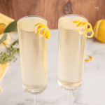 Elderberry French 75 recipe with st Germain, in two champagne flutes, garnished with lemon twists.