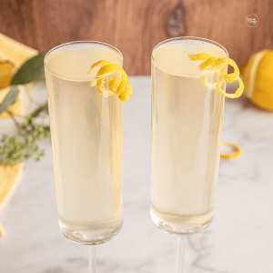 Elderberry French 75 recipe with st Germain, in two champagne flutes, garnished with lemon twists.