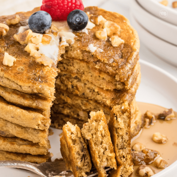 IHOP Harvest grain pancake recipe stacked with wedge cut out, topped with almonds, walnuts and berries.