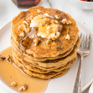 Harvest grain and nut pancake stack on plate, drizzled with maple syrup and pooling butter with chopped walnuts.