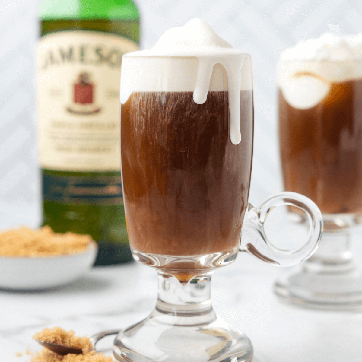 Irish coffee in clear coffee mug with Jameson whiskey bottle in background.