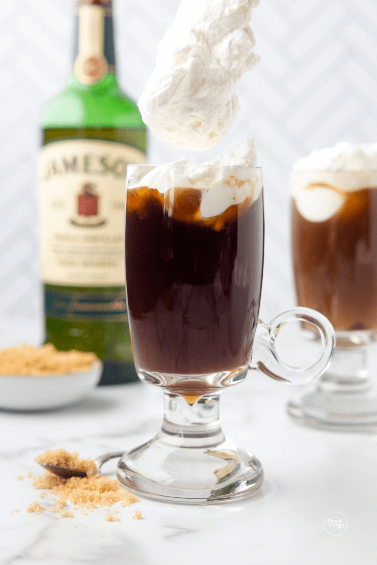 Spooning whipped cream to float on top of hot Irish coffee cocktail.