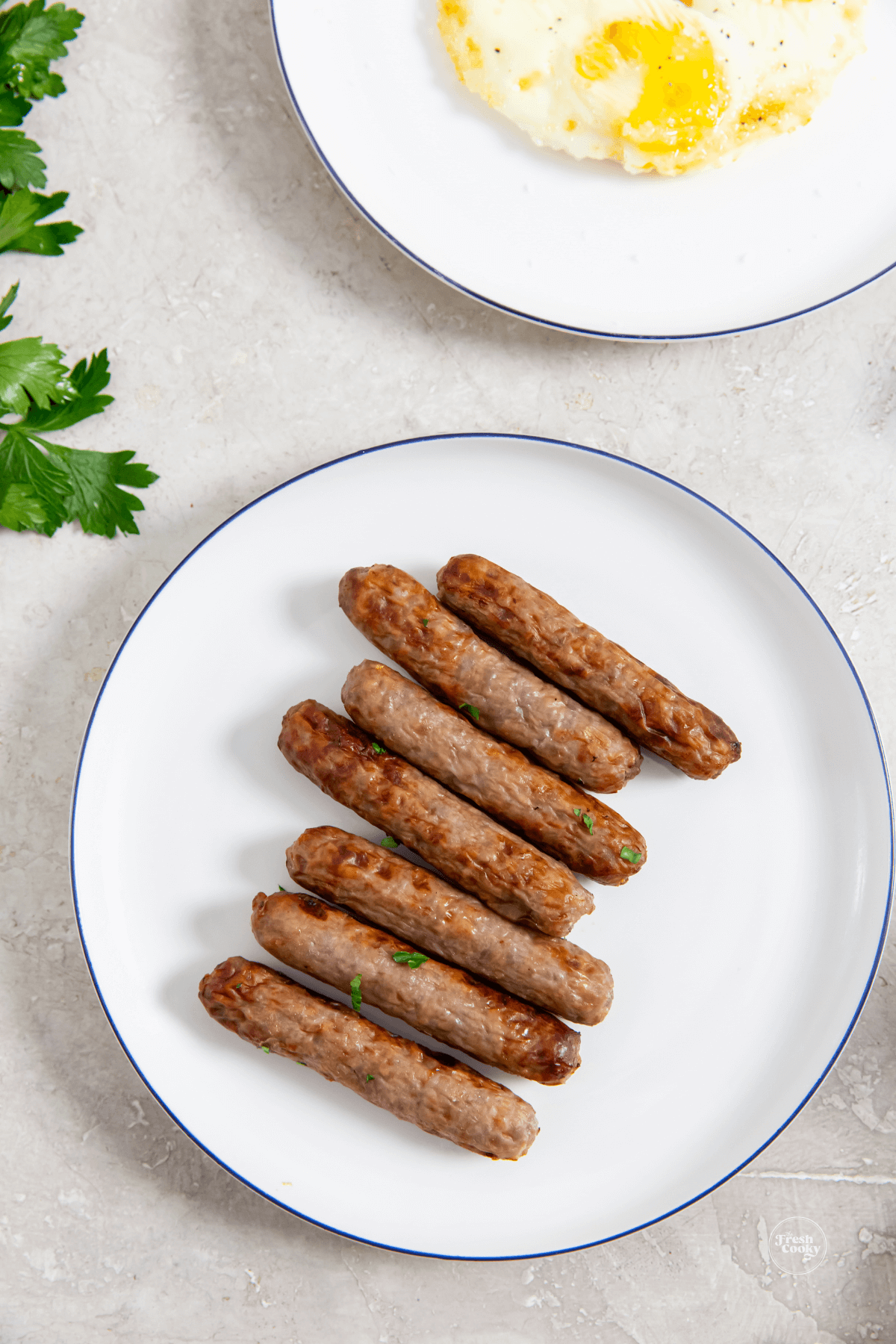 Sausage links on a plate with fried eggs and parsley.