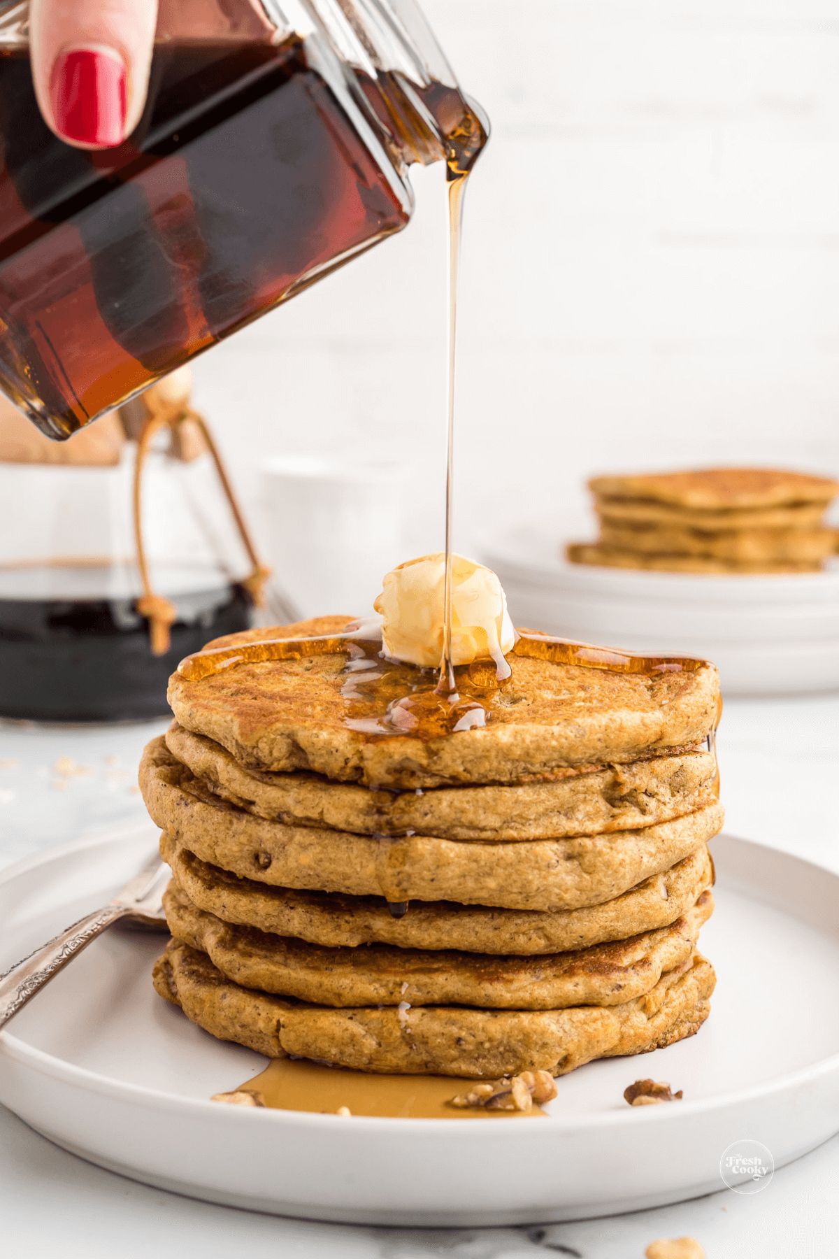 Harvest grain n nut pancakes stack on plate with butter and person pouring maple syrup.