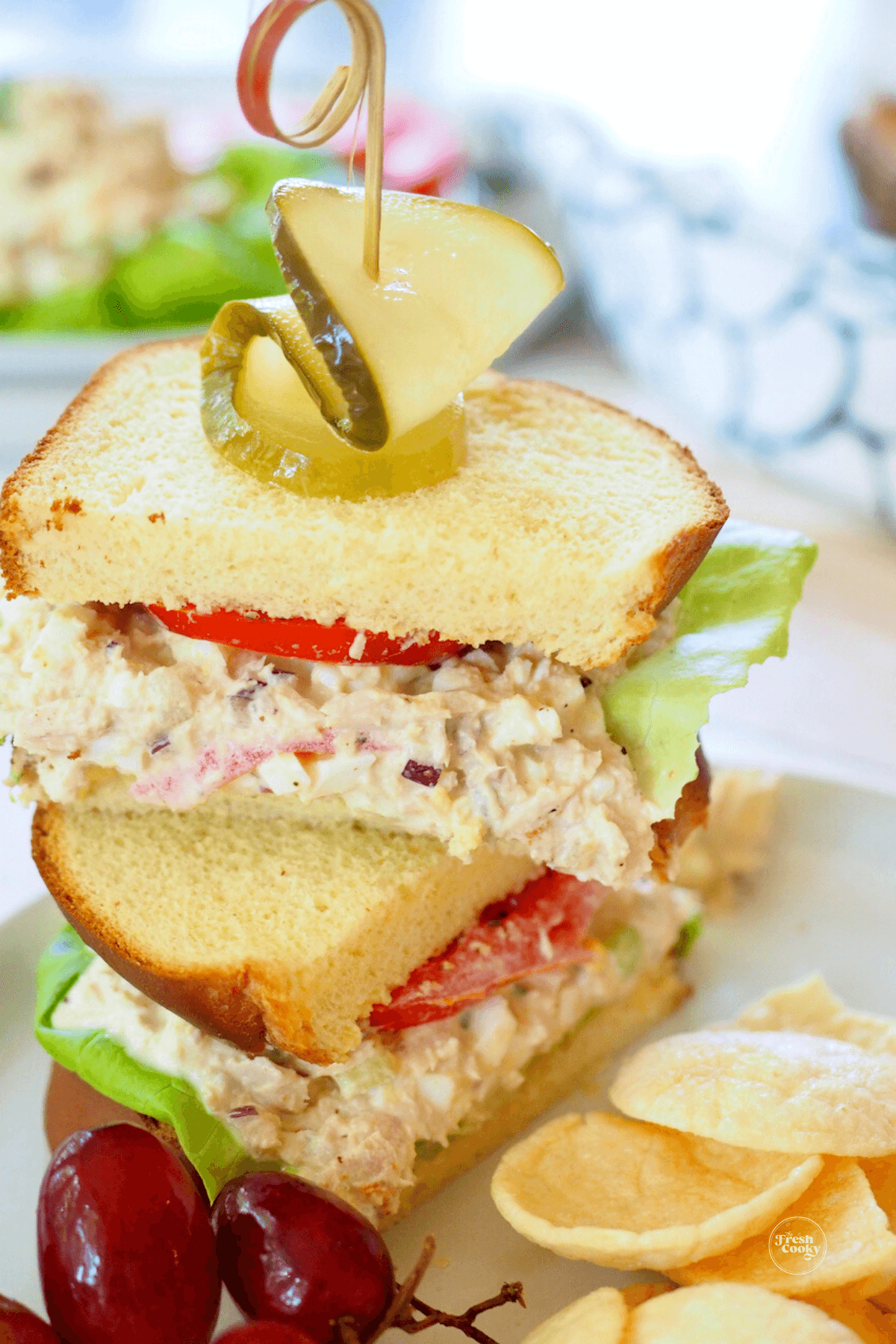 Tuna salad sandwich using brioche bread, served with pickle, chips and red grapes.