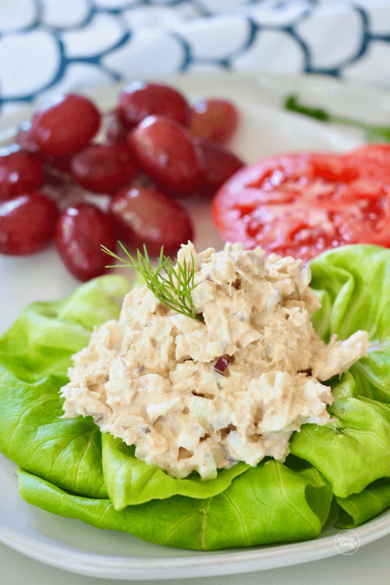 Tuna salad scooped onto butter lettuce leaf and served with grapes and juicy red tomato slices. 