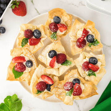 How to make strawberry cheesecake cups, shown on a plate ready to serve, topped with strawberries, blueberries and raspberries.