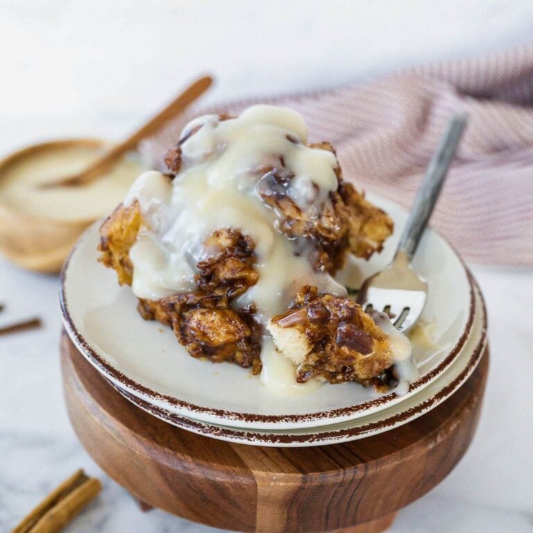 Serving of crockpot cinnamon roll casserole on a plate with frosting.