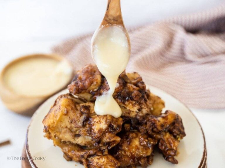 Spooning cream cheese frosting over the top.